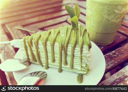 Vintage style matcha cake. Vintage style soft tea leaf embroidered on matcha cake in white plate, placed near a glass of ice green tea on a old wooden table in the evening sunlight