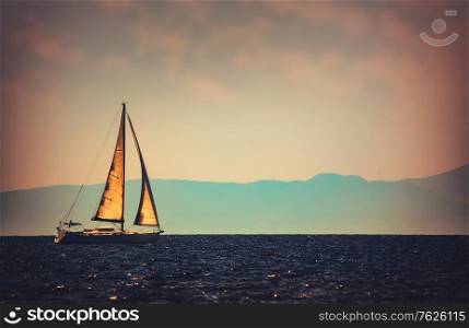 Vintage style photo of a beautiful sailboat in the distance floating in the sea, luxury water sport, wonderful summer adventure
