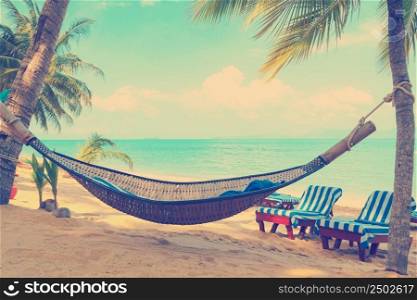 Vintage stylized hammock under palms trees on sunny tropical beach