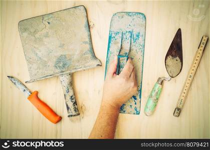 Vintage tone photo of old construction hand tool with worker hand over white wooden background