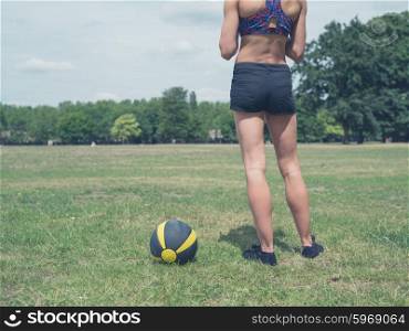 Vintage toned shot of a fit and athletic woman is standing in the park with a medicine ball on a sunny summer day