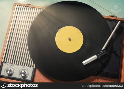 Vintage turntable with a vinyl record on green wooden table, top view and copy space.