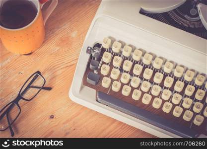 Vintage typewriter, glasses and cup of coffee on a wood desk