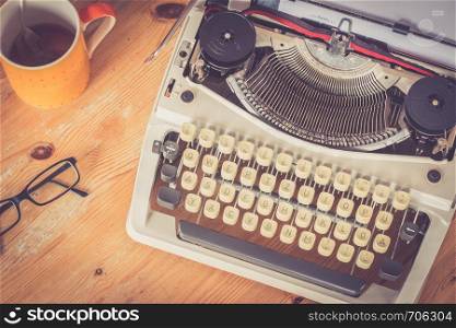 Vintage typewriter, glasses and cup of coffee on a wood desk