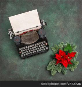 Vintage typewriter with Christmas decoration evergreen tree brunches and red poinsettia flowers. Merry Christmas!