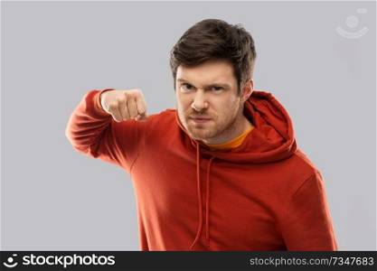 violence, aggression and people concept - angry young man in red hoodie ready for fists punch over grey background. angry young man ready for fist punch
