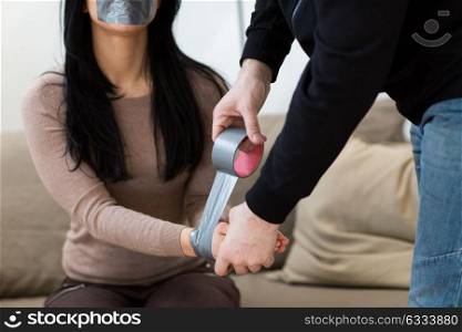 violence, crime, kidnapping and people concept - criminal tying woman hands with adhesive tape (staged photo). criminal tying woman with adhesive tape