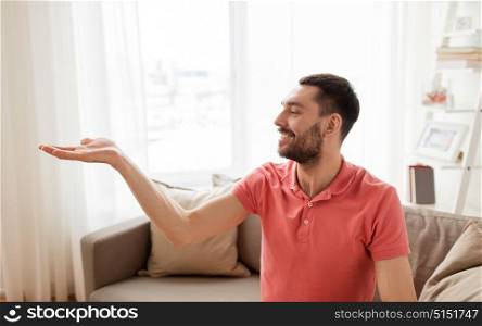 virtual reality, entertainment and people concept - happy man holding something imaginary on palm at home. happy man holding something imaginary at home