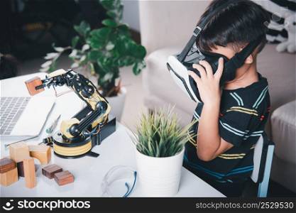 Virtual Reality Simulator. Asian kid boy using VR glasses on robotic arm in workshop, Child learning programer control robot arm with sensors to pick up wood block, Technology education. industry 4.0