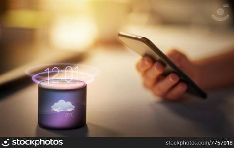 virtual reality, technology and internet of things concept - hand with smartphone and smart speaker with time and weather forecast hologram at night office. hand with smartphone and forecast on smart speaker