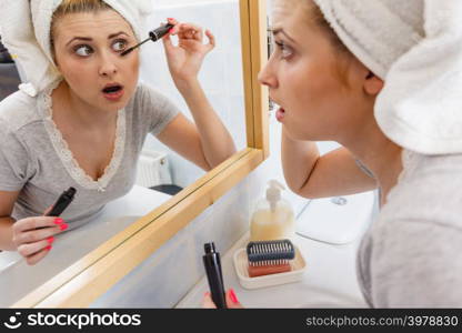 Visage and make up concept. Woman in bathroom wearing towel on head applying mascara on eyelashes. Woman in bathroom applying mascara on eyelashes