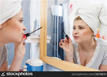 Visage and make up concept. Woman in bathroom wearing towel on head applying mascara on eyelashes. Woman in bathroom applying mascara on eyelashes