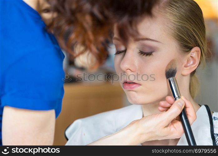 Visage concept. Close up woman getting make up on face. Applying bronzer with brush by professional artist. Woman getting make up done by artist
