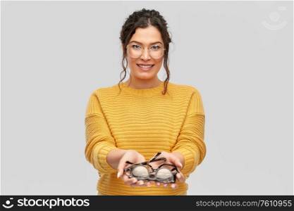 vision, accessory and people concept - portrait of happy smiling young woman with pierced nose holding glasses over grey background. happy smiling young woman with glasses