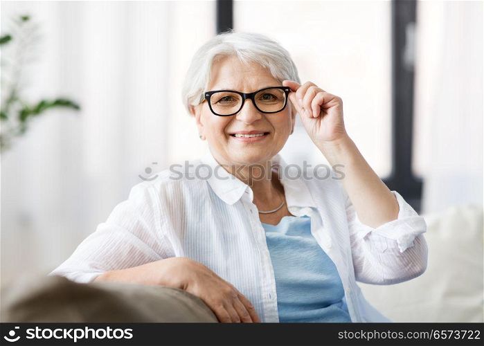 vision, age and people concept - portrait of happy senior woman in glasses sittin on sofa at home. portrait of happy senior woman in glasses at home