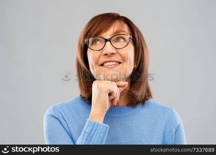 vision and old people concept - portrait of smiling senior woman in glasses looking up and dreaming over grey background. portrait of senior woman in glasses dreaming