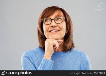 vision and old people concept - portrait of smiling senior woman in glasses looking up and dreaming over grey background. portrait of senior woman in glasses dreaming