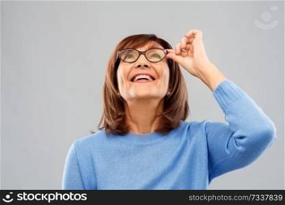 vision and old people concept - portrait of smiling senior woman in glasses looking up over grey background. portrait of senior woman in glasses looking up