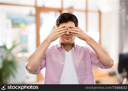 vision and people concept - man closing his eyes by hands over office room background. man closing his eyes by hands over office room