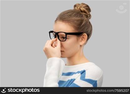 vision and people concept - teenage girl in glasses rubbing nose bridge over grey background. teenage girl in glasses rubbing nose bridge
