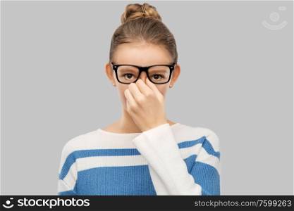 vision and people concept - teenage girl in glasses rubbing nose bridge over grey background. teenage girl in glasses rubbing nose bridge