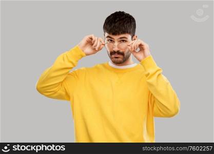 vision and people concept - young man in glasses and yellow sweatshirt over grey background. young man in glasses and yellow sweatshirt