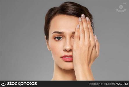 vision, beauty and people concept - beautiful young woman closing one eye with hand over grey background. young woman closing one eye with hand
