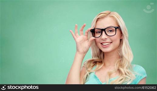 vision, education and people concept - happy smiling young woman or teenage girl glasses over green school chalk board background