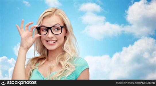 vision, education and people concept - happy smiling young woman or teenage girl glasses over blue sky and clouds background