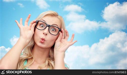vision, education and people concept - happy young woman or teenage girl glasses making funny fish face over blue sky and clouds background