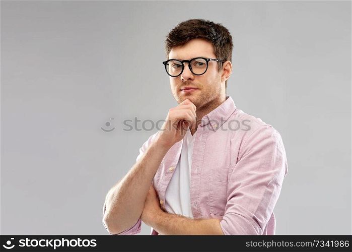 vision, education and people concept - thinking young man in glasses over grey background. thinking young man in glasses over grey background