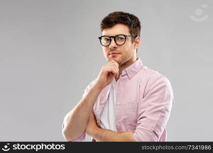 vision, education and people concept - thinking young man in glasses over grey background. thinking young man in glasses over grey background