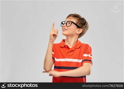 vision, education and school concept - portrait of happy smiling boy in eyeglasses and red polo t-shirt pointing finger up over grey background. portrait of happy smiling boy in eyeglasses