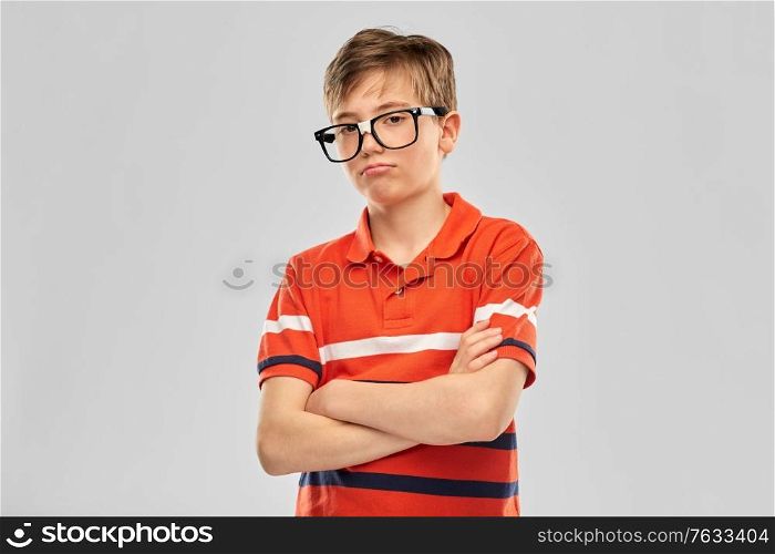 vision, education and school concept - portrait of sad boy in eyeglasses and red polo t-shirt crossed arms over grey background. portrait of sad boy in eyeglasses