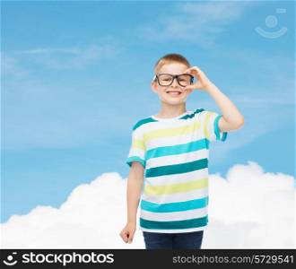 vision, education, childhood and school concept - smiling little boy in eyeglasses over blue sky with white cloud background