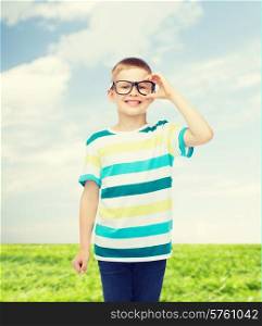 vision, education, nature and school concept - smiling little boy in eyeglasses over natural background