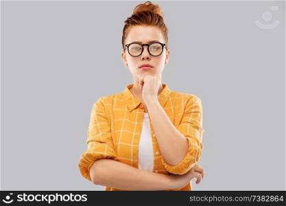 vision, education people concept - serious thinking red haired teenage student girl in glasses and checkered shirt over grey background. thinking redhead teenage student girl in glasses