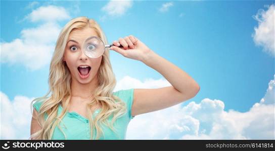 vision, exploration, investigation, education and people concept - happy smiling young woman or teenage girl looking through magnifying glass over blue sky and clouds background