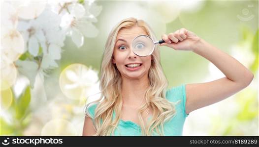 vision, exploration, investigation, education and people concept - happy smiling young woman or teenage girl looking through magnifying glass over natural spring cherry blossom background
