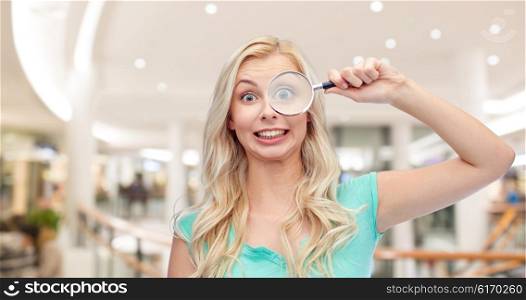 vision, exploration, investigation, education and people concept - happy smiling young woman or teenage girl looking through magnifying glass over mall or shopping center background