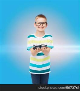 vision, health and people concept - smiling little boy in eyeglasses holding spectacles over blue background with laser light