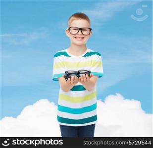vision, health and people concept - smiling little boy in eyeglasses holding spectacles over blue sky with white cloud background