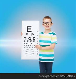 vision, health, childhood, ophthalmology and people concept - smiling little boy in eyeglasses with with eye chart over blue background with laser light