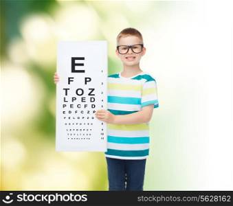 vision, health, ecology, ophthalmology and people concept - smiling little boy wearing eyeglasses with white blank board over green background