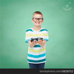 vision, health, education, childhood and people concept - smiling little boy in eyeglasses holding spectacles over green board background