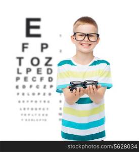 vision, health, ophthalmology and people concept - smiling little boy in eyeglasses holding spectacles over eye chart background