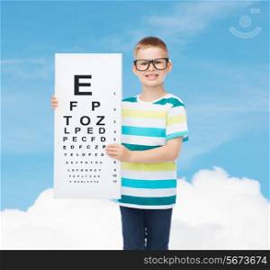 vision, health, ophthalmology, childhood and people concept - smiling little boy in eyeglasses with eye chart over blue sky background