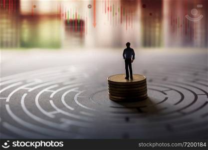 Vision of Leader in Financial or Economy Crisis Concept. Stock Marketing Graph is going Crash and Down. Miniature Figure of Businessman standing on Money Coin Stack at the center of Maze and Looking Forward