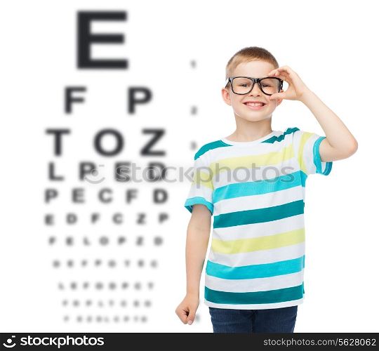 vision, ophthalmology and childhood concept - smiling little boy in eyeglasses over eye chart background