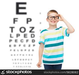 vision, ophthalmology and childhood concept - smiling little boy in eyeglasses over eye chart background